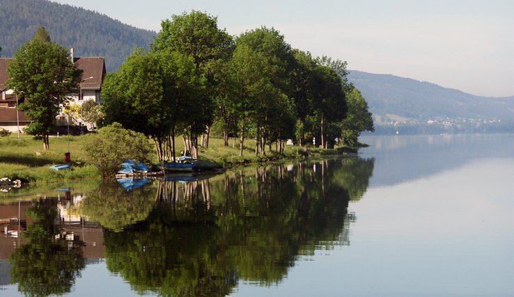 Rive du lac de Joux, avec petite maison, quelques arbres et quelques bateaux amarrés.