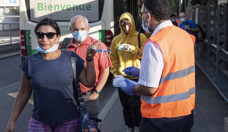 Un homme portant gants en latex et gilet fluorescent distribue des masques aux passants près de la gare de Morges.