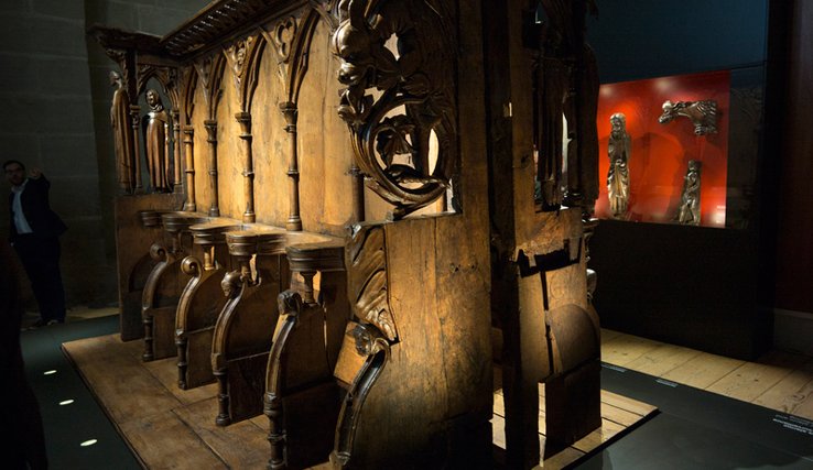Les stalles de bois sculpté sous un éclairage calculé. Au fond, dans une vitrine, d'autres objets anciens en bois sculpté.