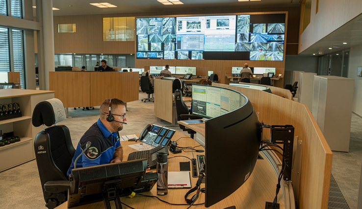 Un opérateur à son poste de travail dans la grande salle de la centrale d'alarme. Au fond, un mur d'écrans avec des informations et images du trafic routier.