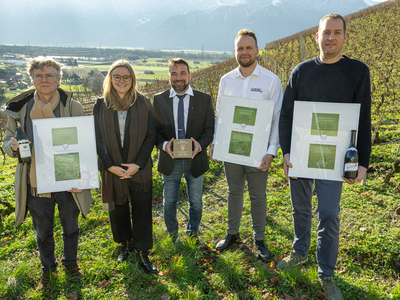 Les personnes posent dans une vigne d'Yvorne en tenant leurs distinctions. Derrière, le paysage de la plaine du Rhône.