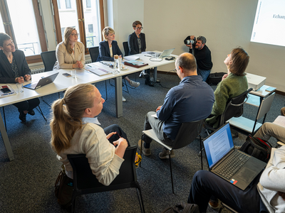 Scène de conférence de presse. Les quatre personnes assises face à des journalistes. Au fond, un photographe au travail.