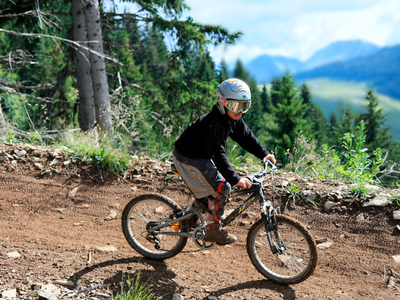 un homme sur un VTT descend une pente dans une forêt. au loin, les montagnes