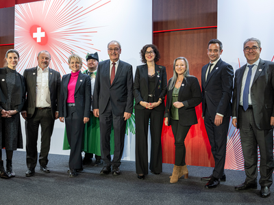 Les personnes posent devant un décor orné d'une croix nationale stylisée.