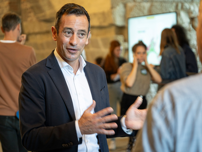 Le conseiller d'Etat parle à un journaliste, debout, les mains écartées.